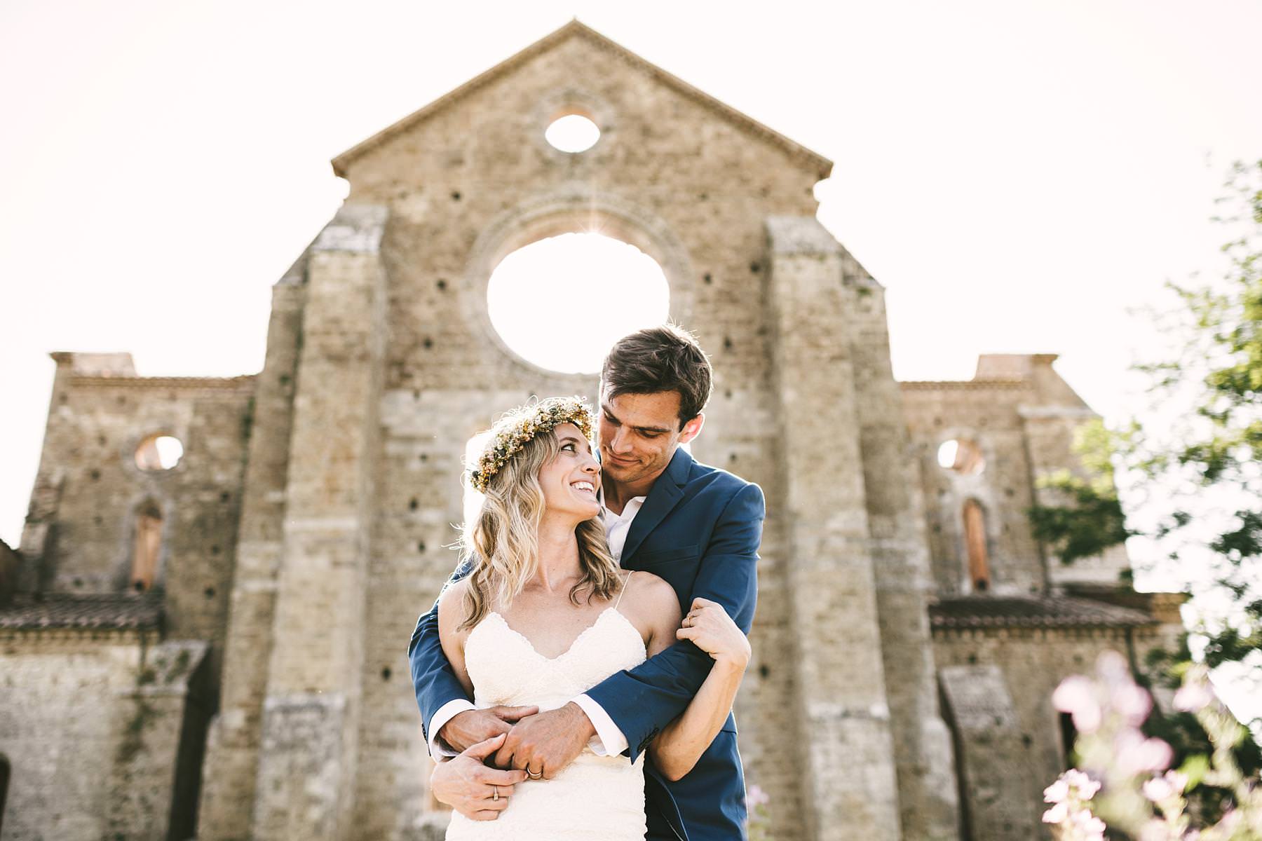 Unforgettable bride and groom wedding portrait at the Roofless Abbey of San Galgano full of colours, light, architecture and love gestures. Intimate destination Italian civil wedding in Tuscany