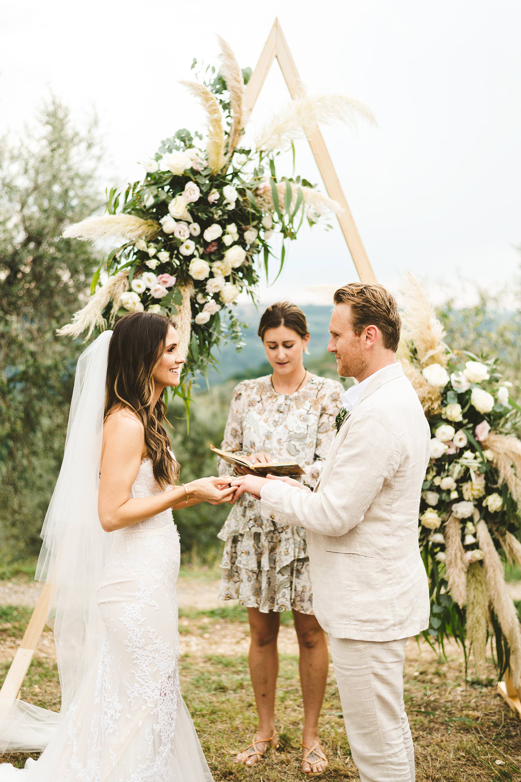 Lovely outdoor symbolic wedding ceremony decor with triangular shape as a stunning frame that witnessed bride and groom promises of love. Modern and unusual wedding framed by the olive groves of Chianti