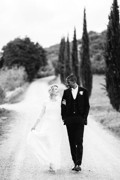 La sposa Isabella nel suo abito Laure De Sagazan e lo sposo Tanaka nel suo abito Hugo Boos passeggiano per la dimora storica del Montelucci Country Resort, incorniciata dalla pittoresca stradina di cipressi e dal vigneto. Matrimonio nella campagna toscana tra il Chianti e il Valdarno