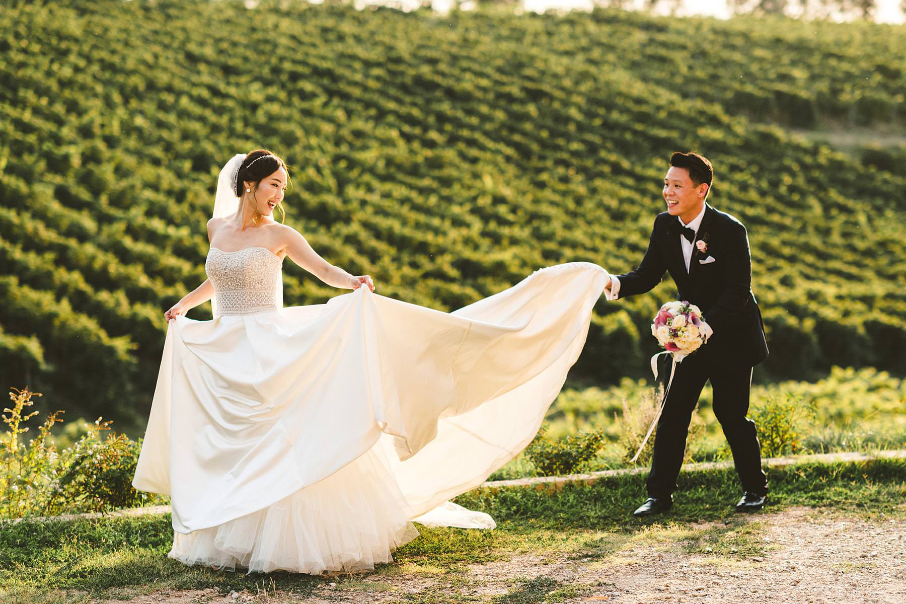 Wedding photo in around the vineyard surrounding Castello Il Palagio a typical scenery of Chianti in Tuscany. Bride in Maggie Sottero elegant gown and groom in Indochino suit