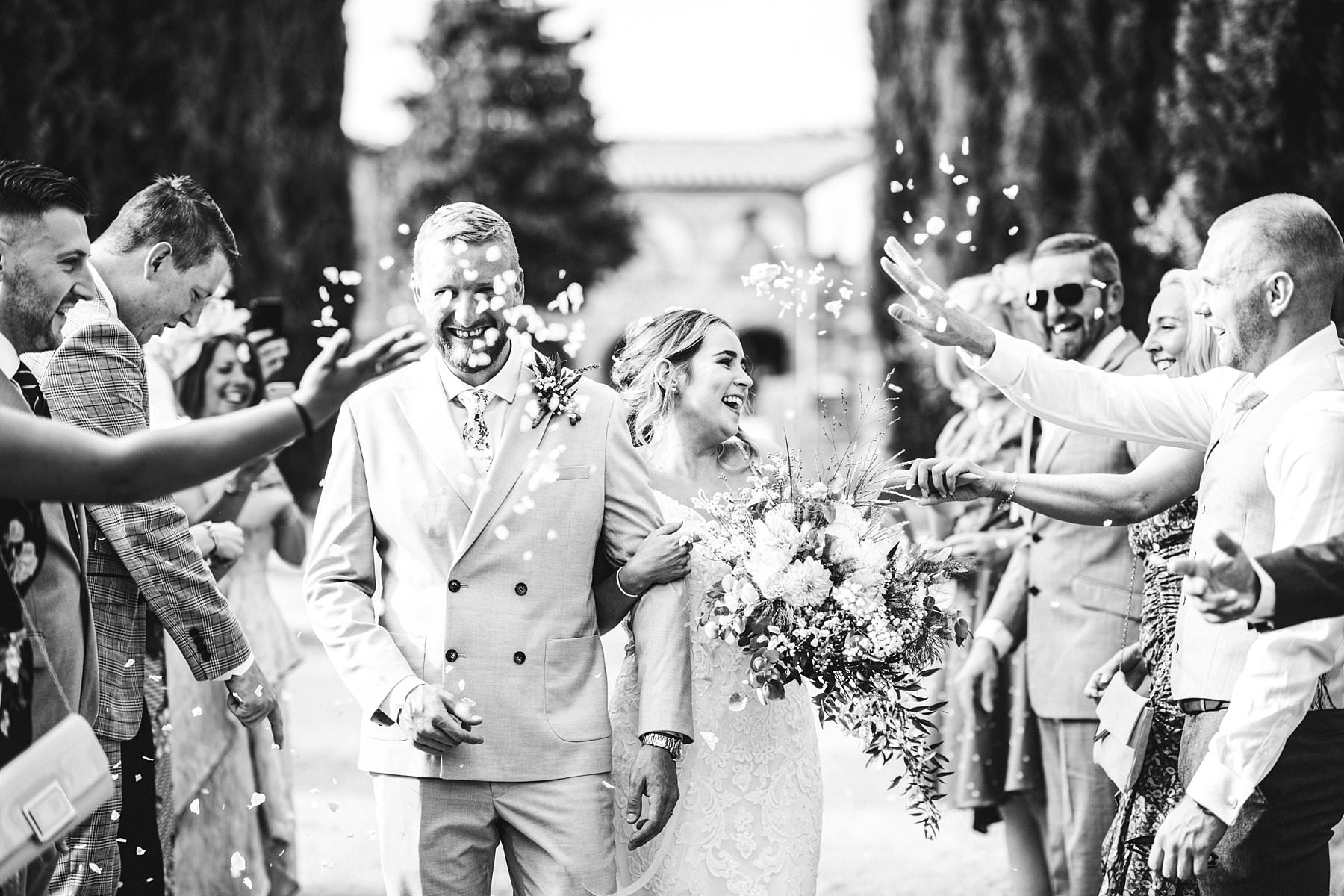 Sam and Jerry, two lovely souls and a small wedding abroad. Joyful explosion of white flower petals in front of the astounding venue Villa Boscarello in the countryside of Tuscany in Val d’Orcia area