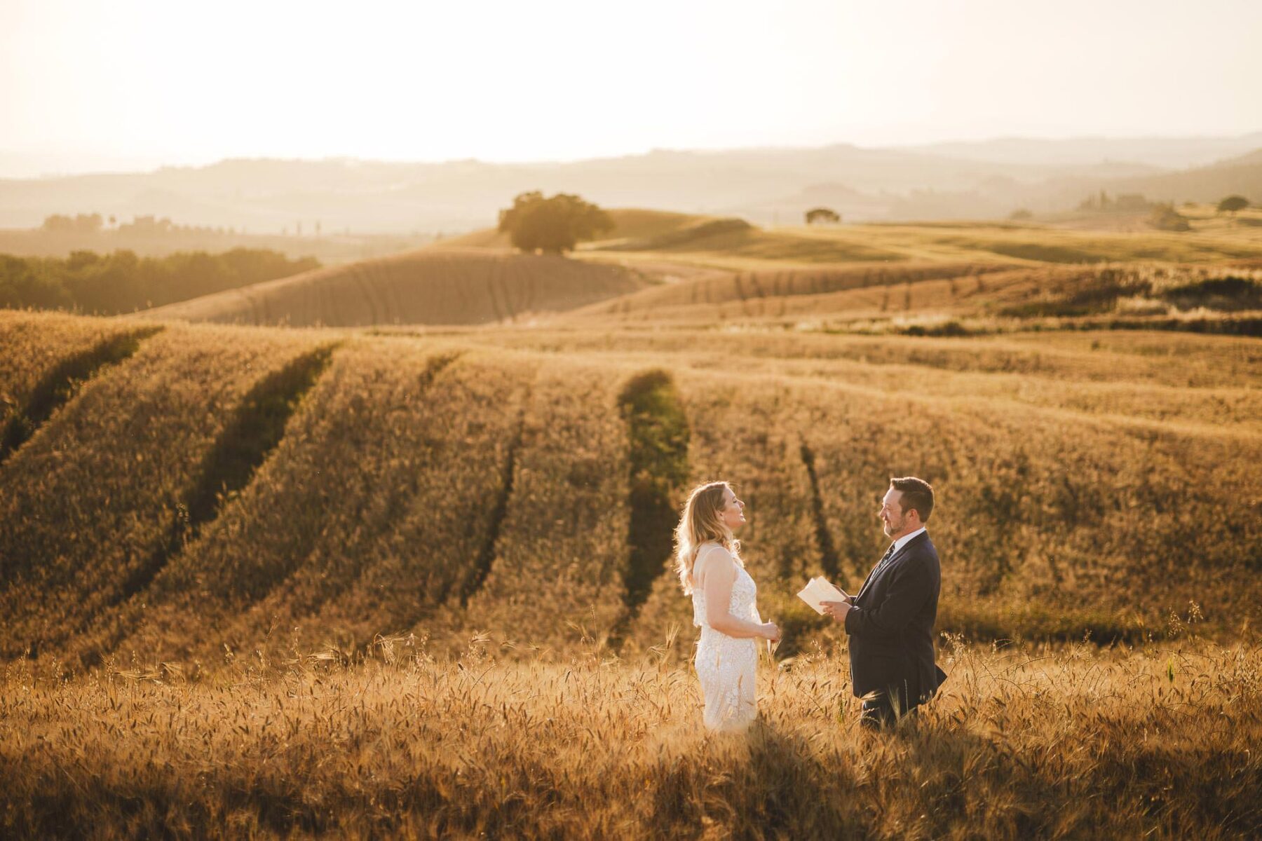 Dreaming and evocative bride and groom Tuscan elopement photo in heart of Val d'Orcia countryside near Pienza at golden hour into a beautiful grain field