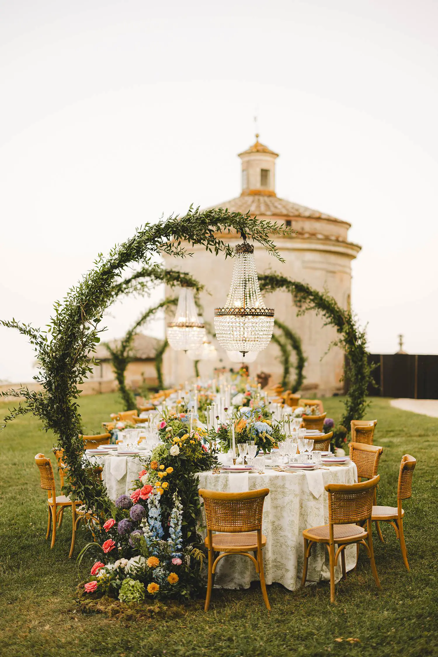 A dreamy long-table wedding look cascading florals, woven chairs, chandeliers floating above the greenery, and the softest evening light at Castello di Celsa
