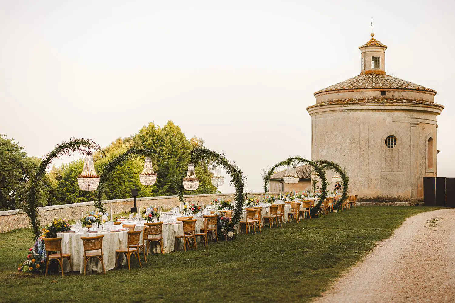 A dreamy long-table wedding look cascading florals, woven chairs, chandeliers floating above the greenery, and the softest evening light at Castello di Celsa