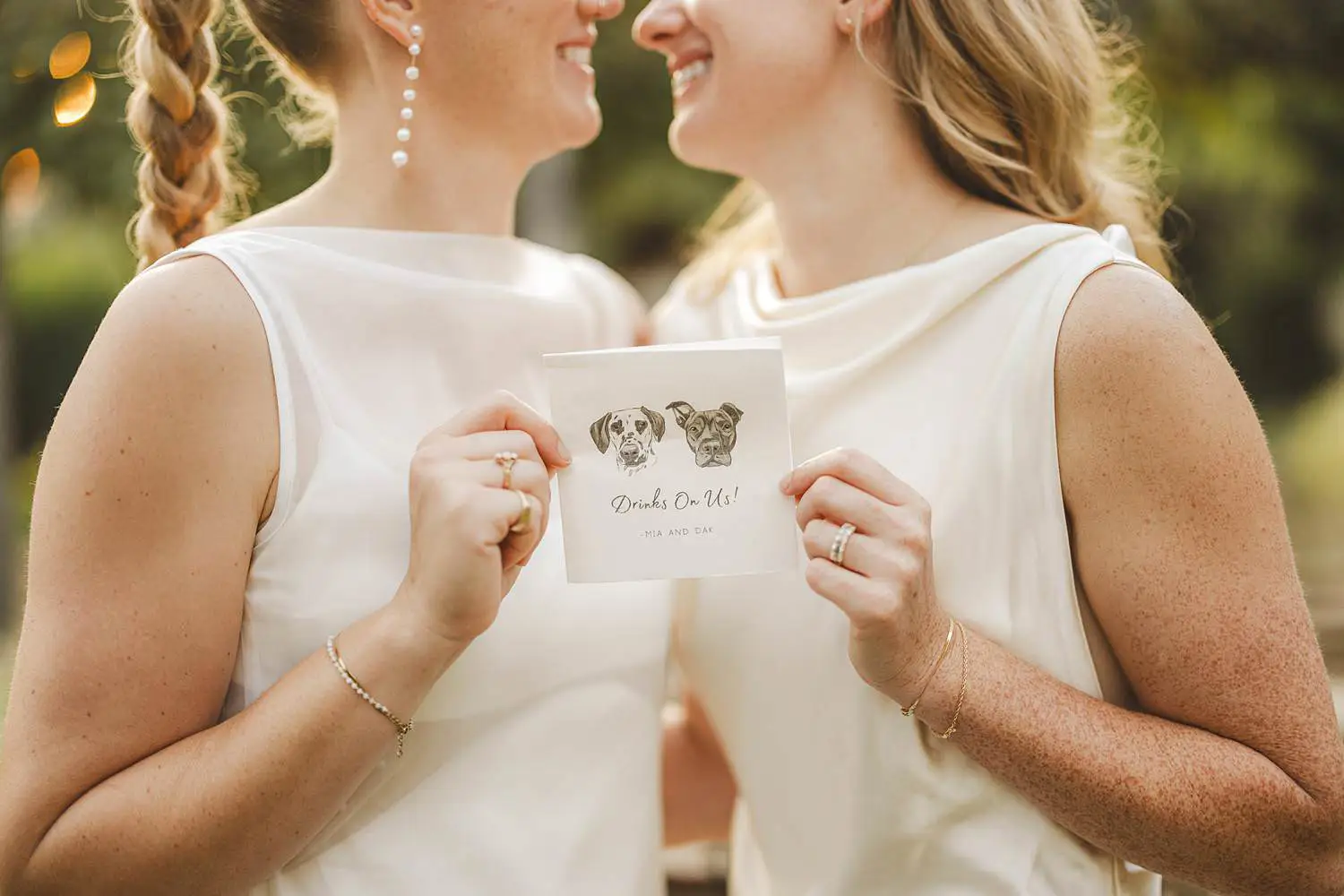 Two brides smiling while holding a napkin featuring illustrations of their dogs at a same sex wedding at Borgo di Petrognano in Tuscany