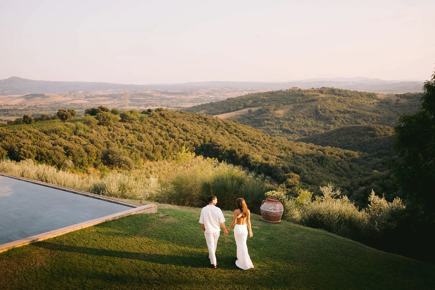 Elegant couple walking beside the pool overlooking the evocative Tuscan rolling hills at Castello di Vicarello.