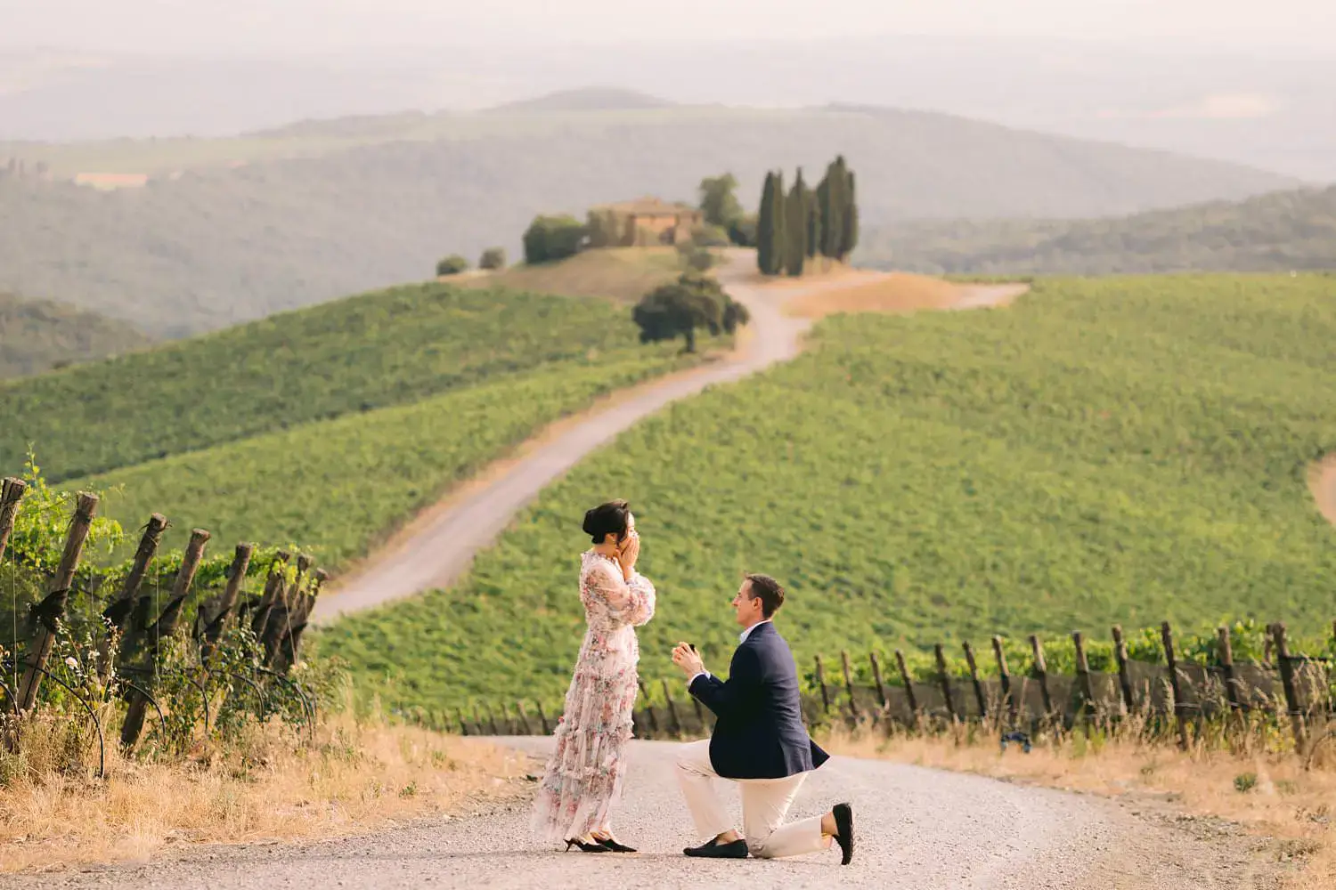 A man kneels to propose to his partner on the winding road above Capanna vineyard at Rosewood Castiglion del Bosco, Tuscany.