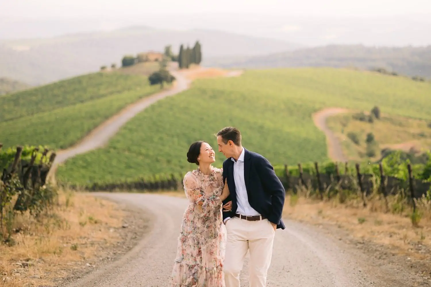 A newly engaged pair leans close on a winding road, framed by Capanna’s vineyards and distant cypress trees.