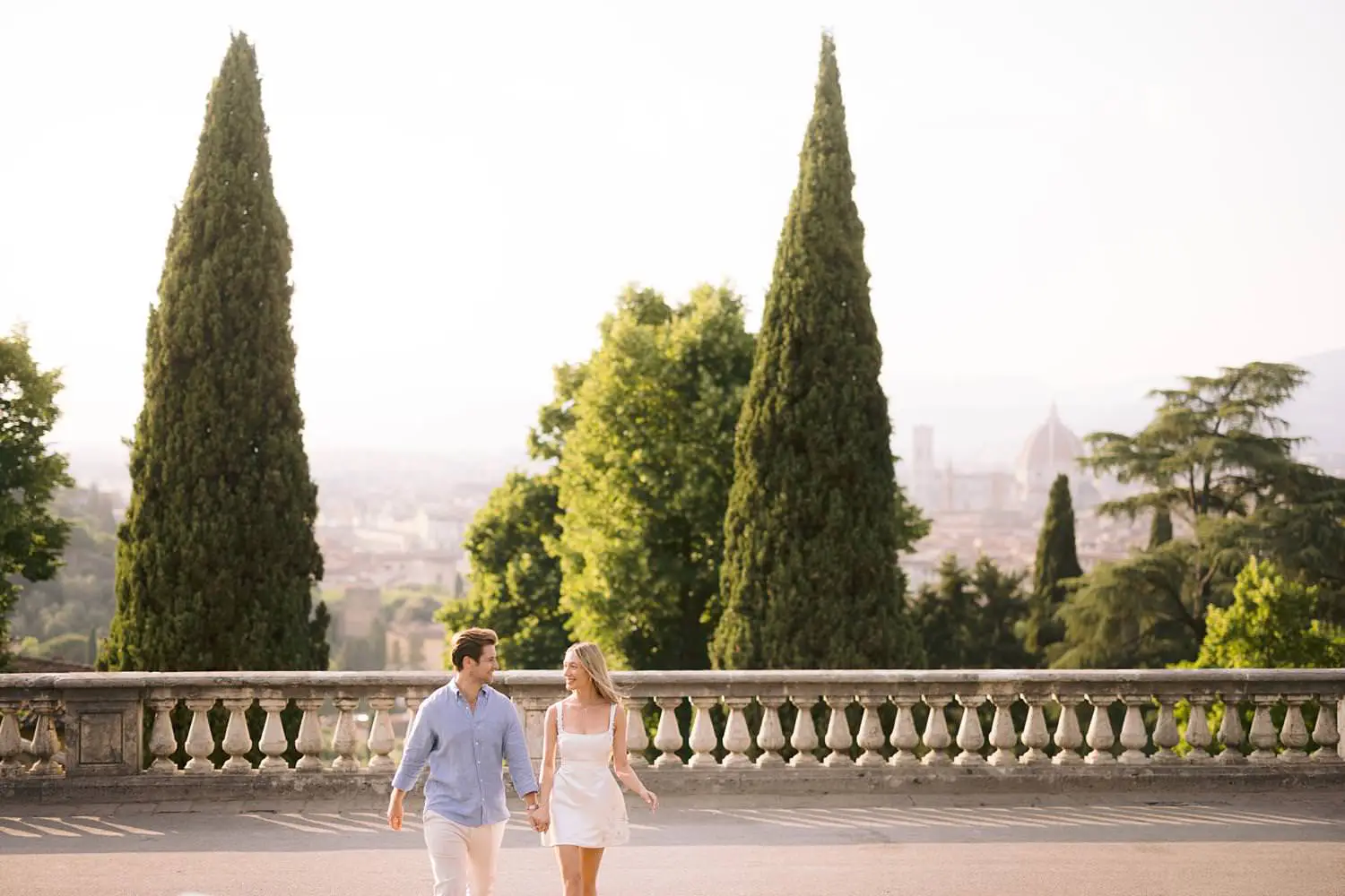 Couple walking at San Miniato al Monte with cypress trees and the Florence skyline behind them.