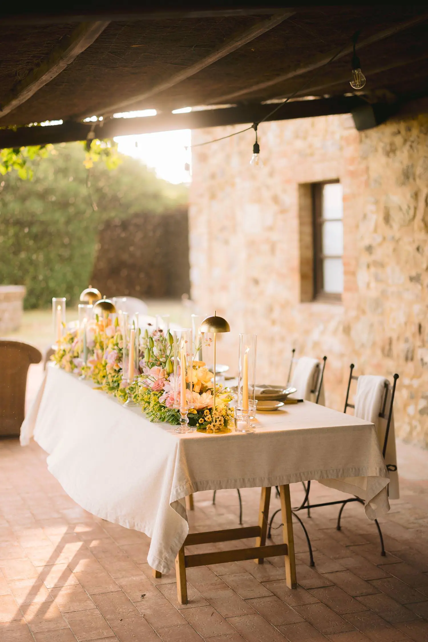 An intimate dinner table dressed with flowers, candles and linen beneath the timber portico of Capanna House.