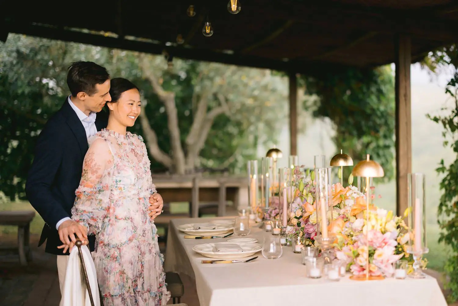The newly engaged pair stands beside a table dressed with pastel flowers and candles at Capanna House, Rosewood Castiglion del Bosco.