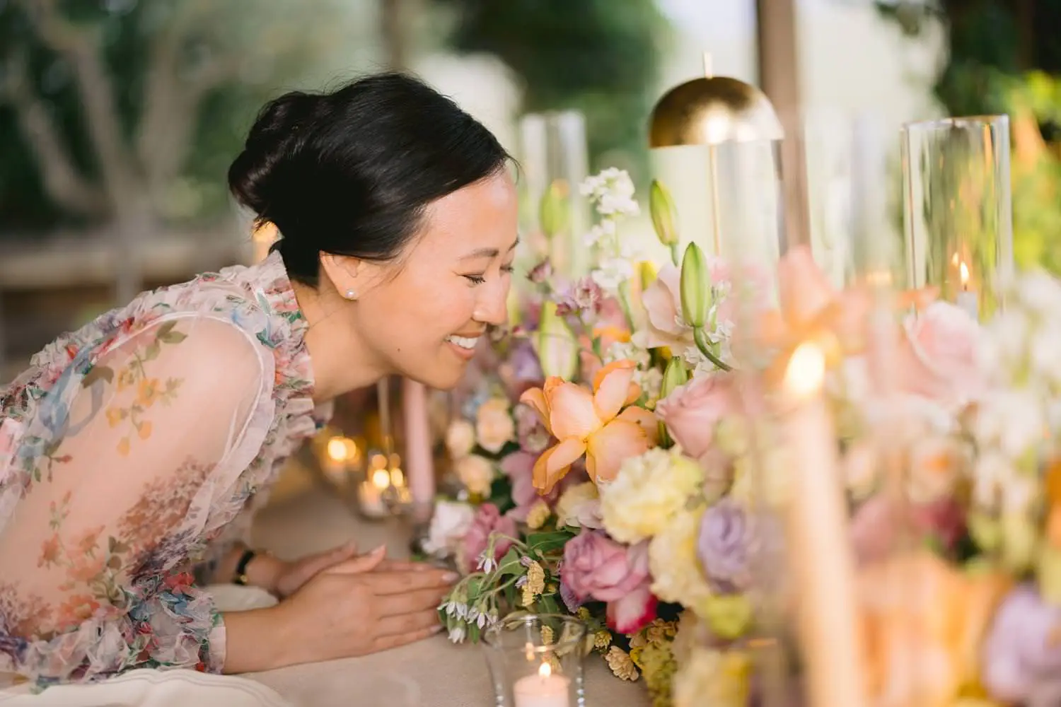 A woman leans toward pastel flowers at the private dinner table, her floral dress echoing the colours of the arrangements at Capanna House.