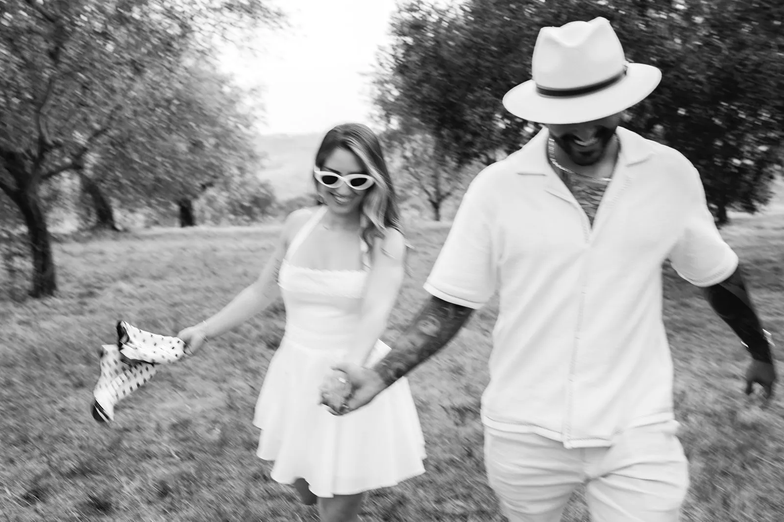 Black-and-white photograph with motion blur of Nere and Leo walking hand in hand among olive trees in Chianti.