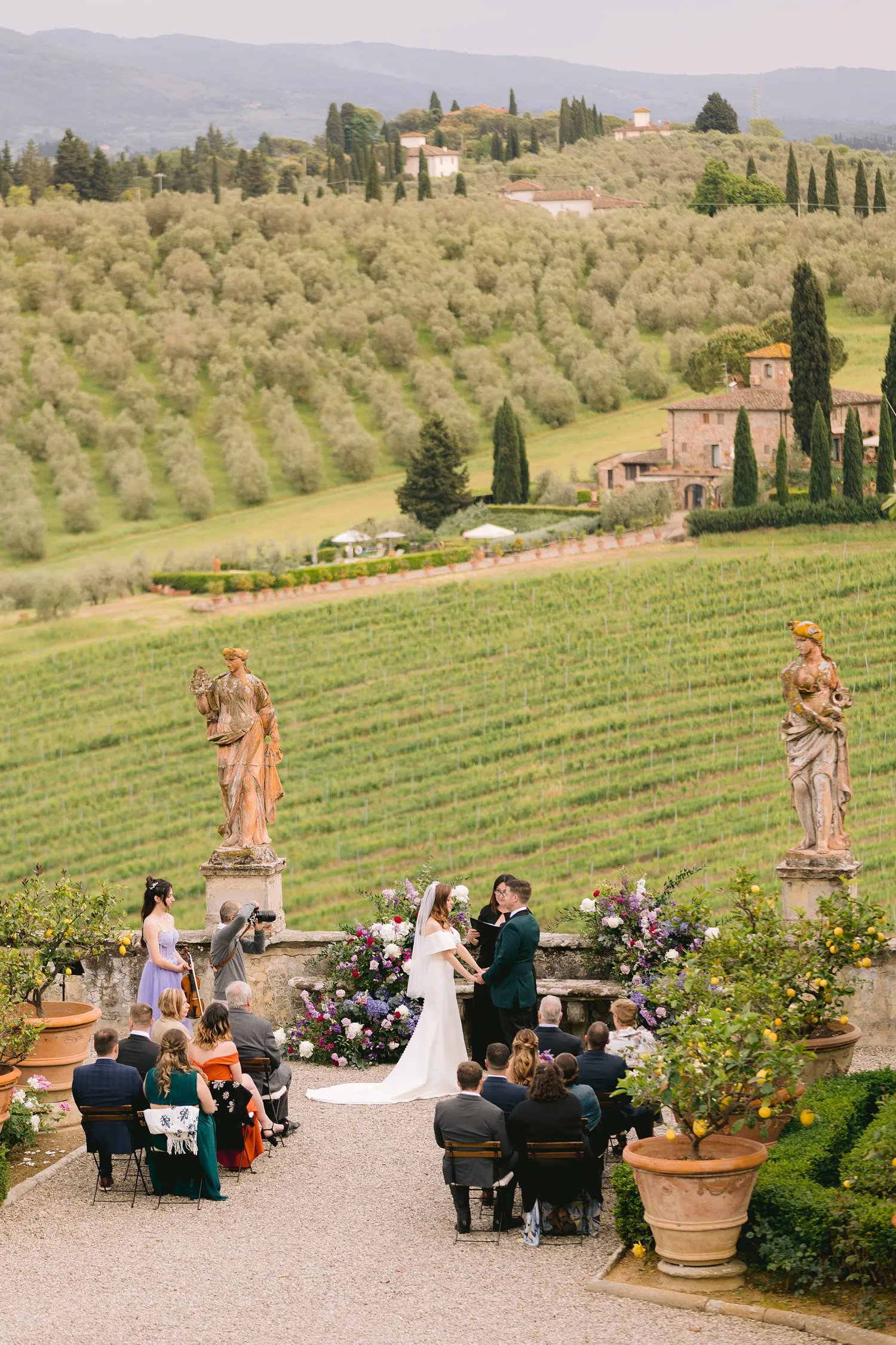 Elevated view of Kathryn and Kevin's outdoor ceremony at Villa Corsini, with guests seated between statues and olive groves across the hills.