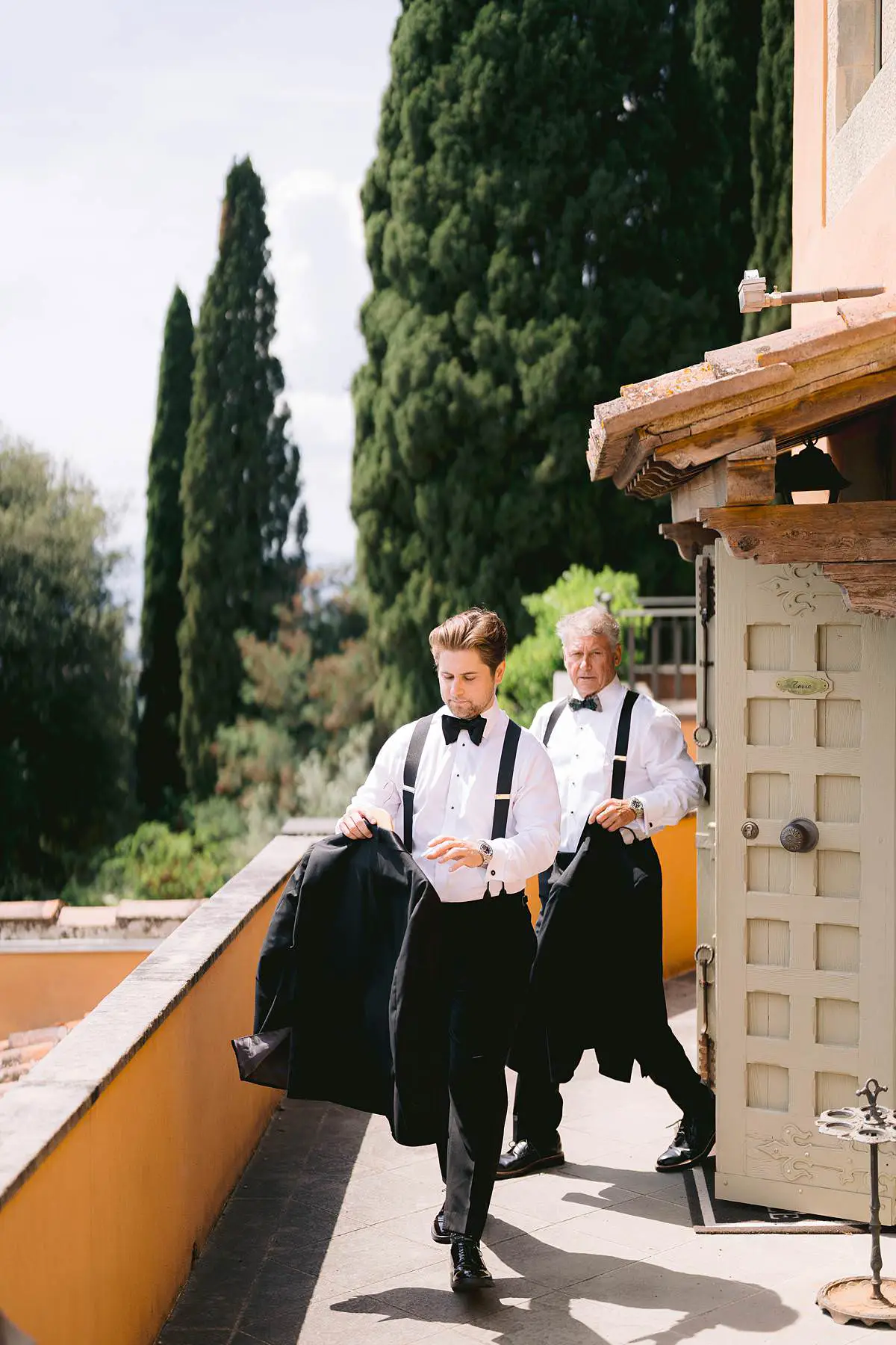 Groom and his father carry their tuxedo jackets outside Villa Le Fontanelle.
