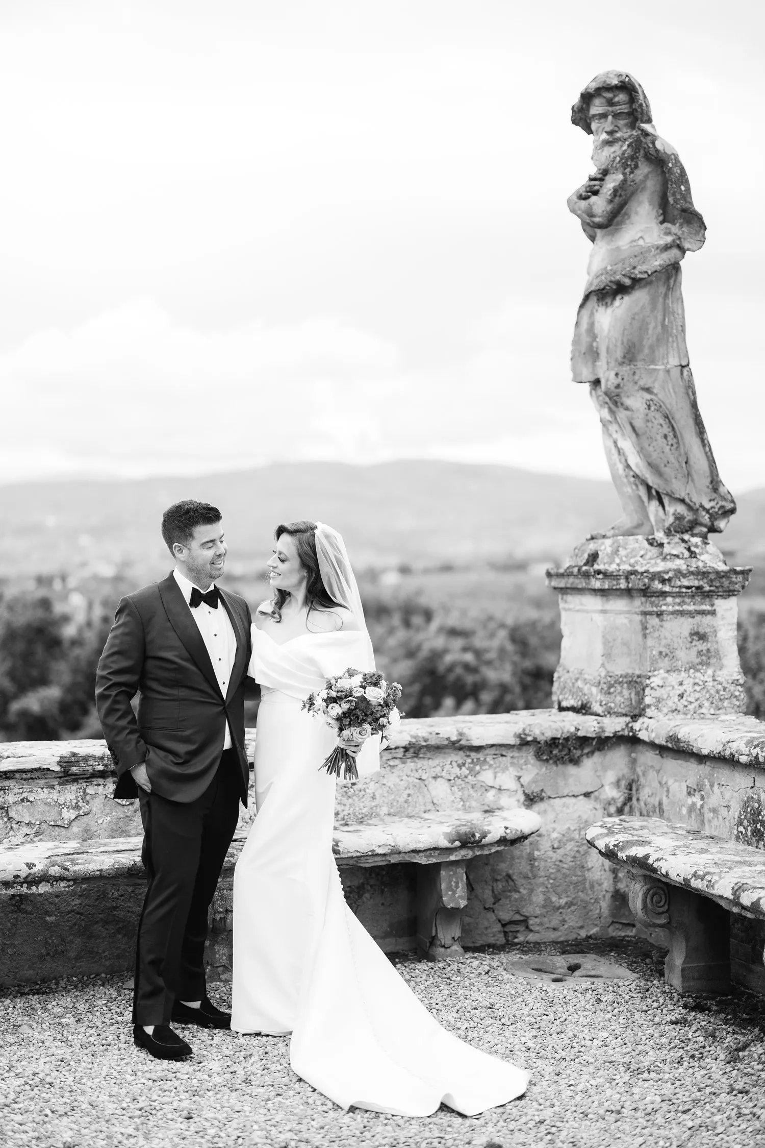 Black-and-white photograph of Kathryn and Kevin looking at each other beside a stone balustrade and statue in the gardens of Villa Corsini.