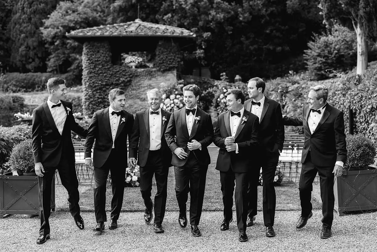 Groom and groomsmen in tuxedos walk through the Villa Le Fontanelle ceremony garden.