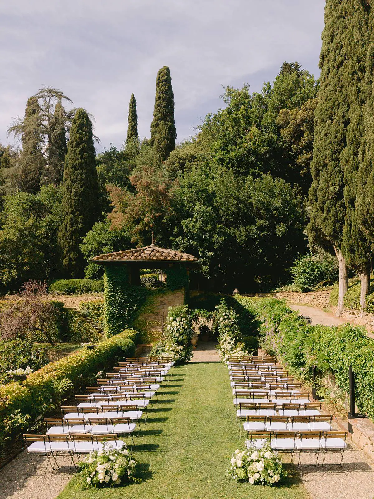 The garden ceremony setup at Villa Le Fontanelle in Florence, framed by cypress trees and white flowers.