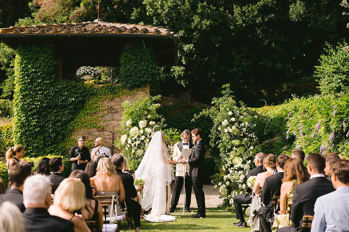 Madison and Travis exchange vows during an outdoor ceremony framed by white floral arches at Villa Le Fontanelle in Florence.