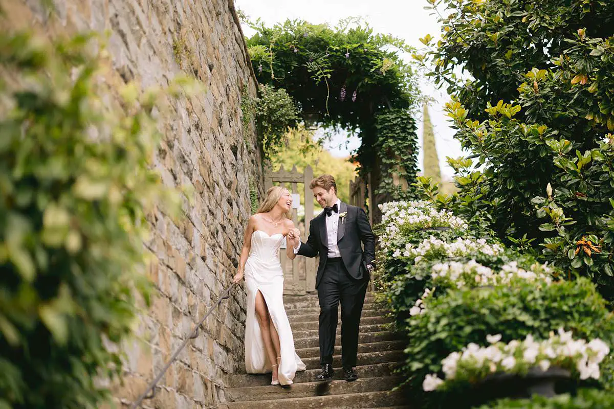Madison and Travis walk hand in hand along a flower-lined stone path at Villa Le Fontanelle.