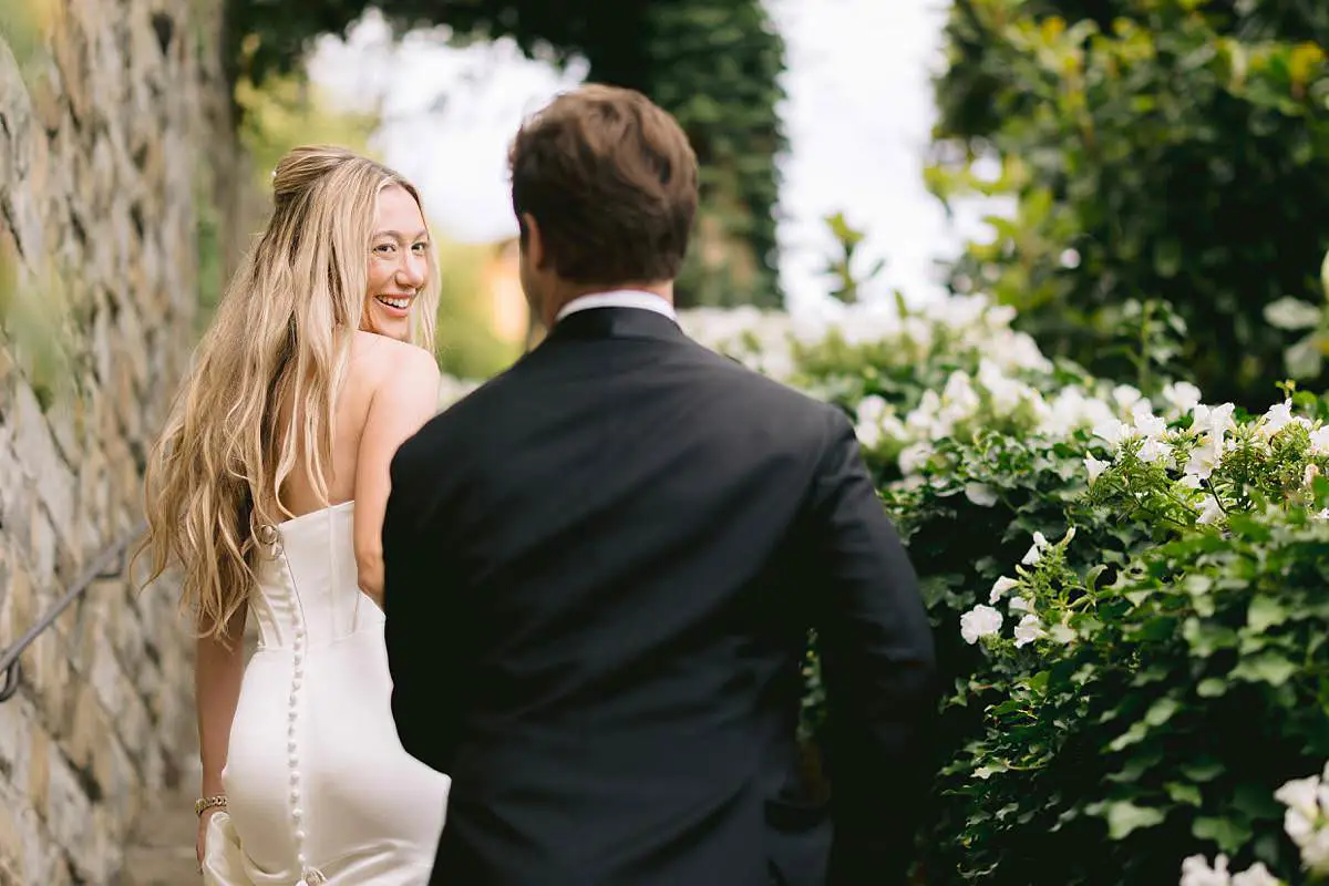 Bride smiles back at the camera while walking with the groom through the Villa Le Fontanelle garden.
