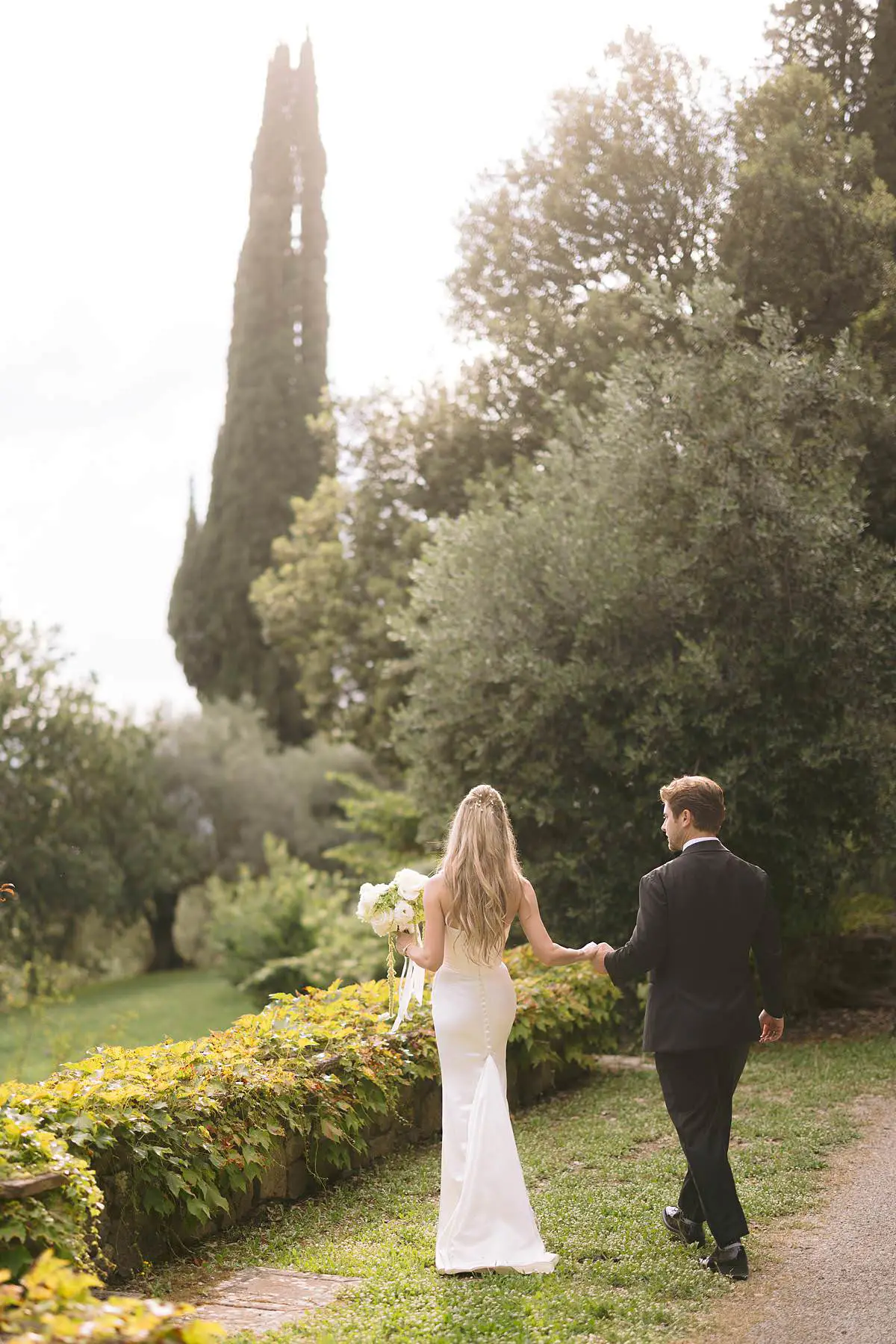 Madison and Travis walk hand in hand through the cypress-lined garden at Villa Le Fontanelle.