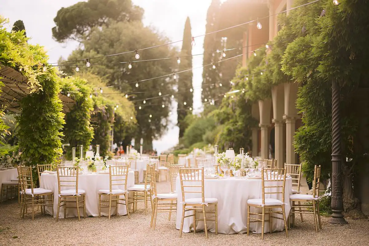 Round reception tables with white flowers and gold chairs beneath garden lights at Villa Le Fontanelle in Florence.